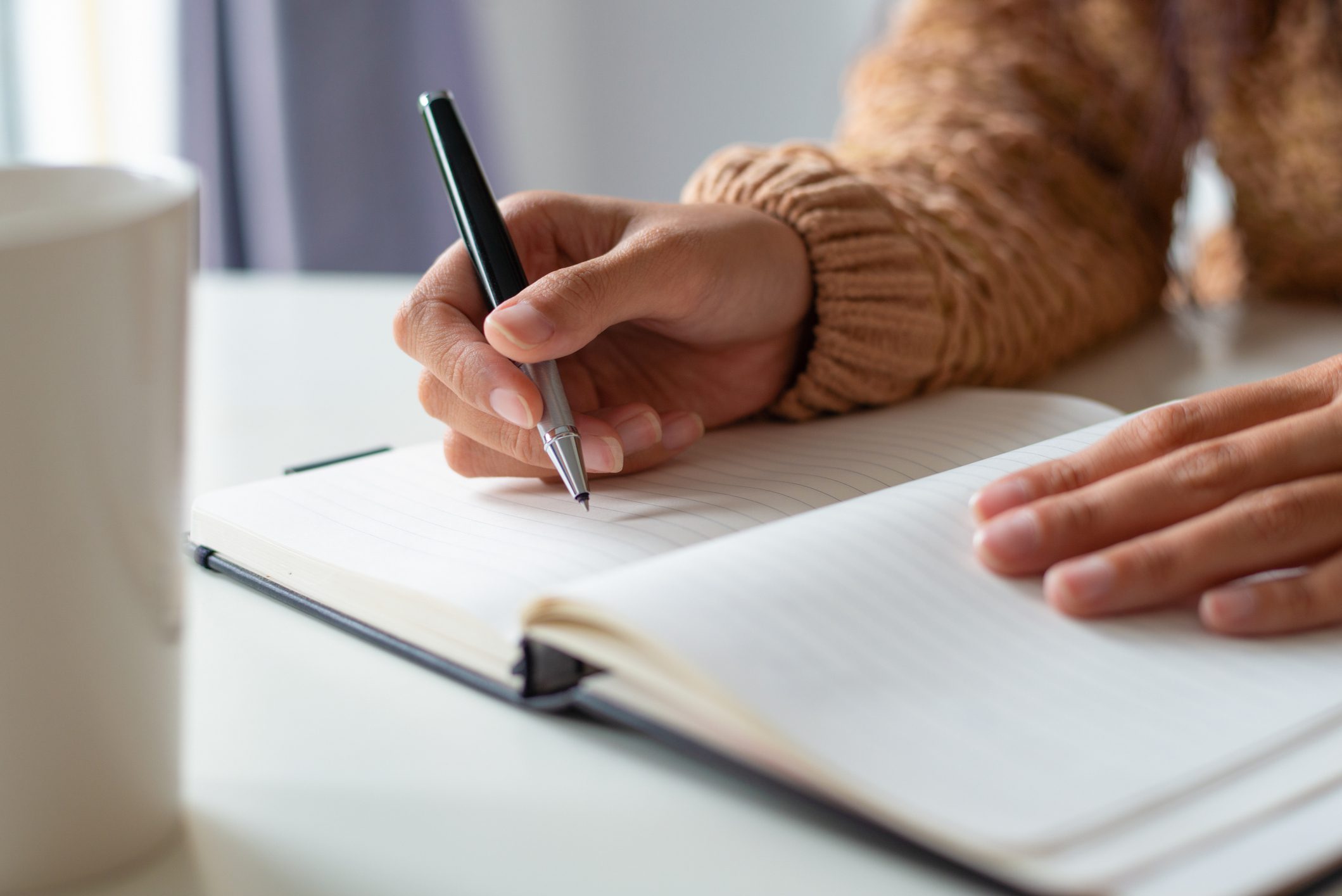 Close-up of woman sitting at table and planning schedule. Unrecognizable lady making notes in diary. Tasks concept