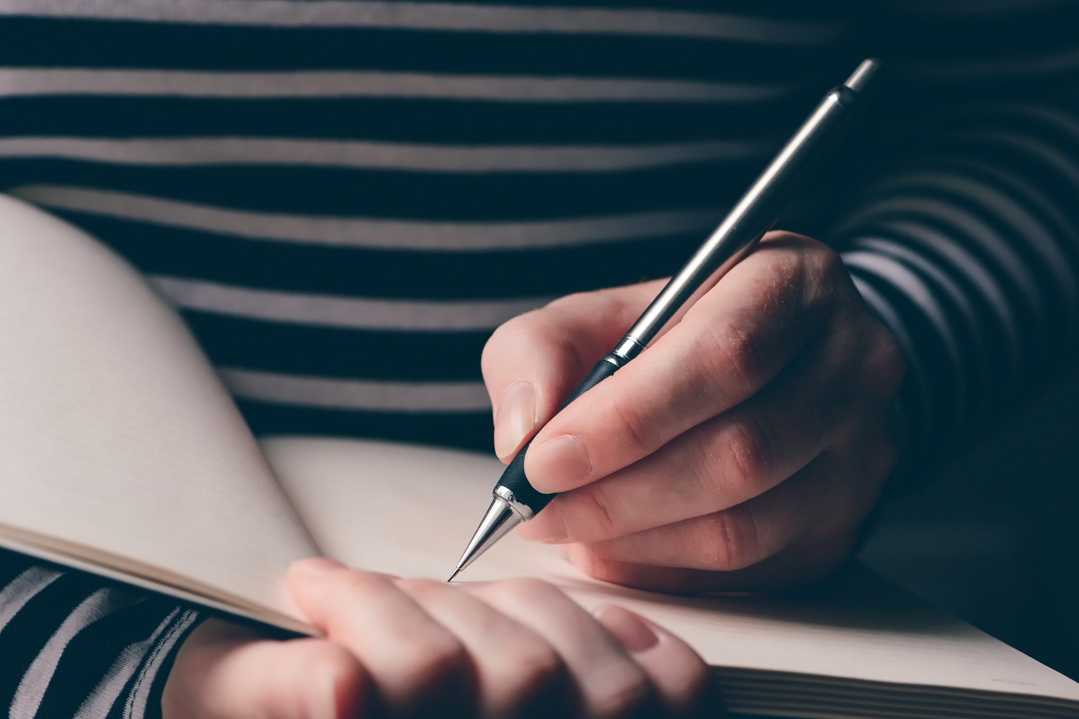 Left-handed woman writing diary, close up of hands with pencil and notebook