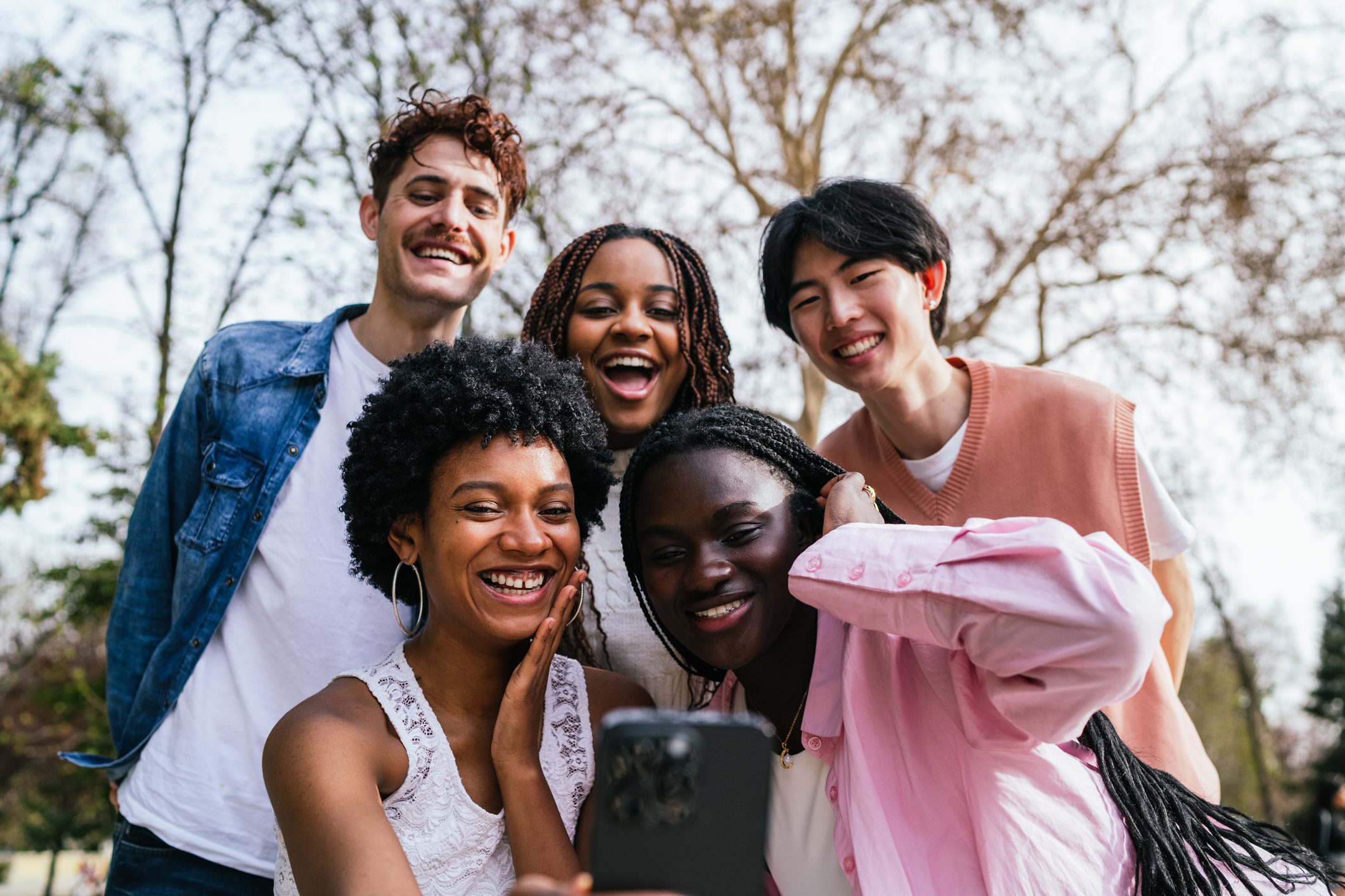A group of young multiethnic people are smiling and taking a selfie with a cell phone. Scene is happy and fun, as the group of friends are enjoying each other's company and capturing a moment together